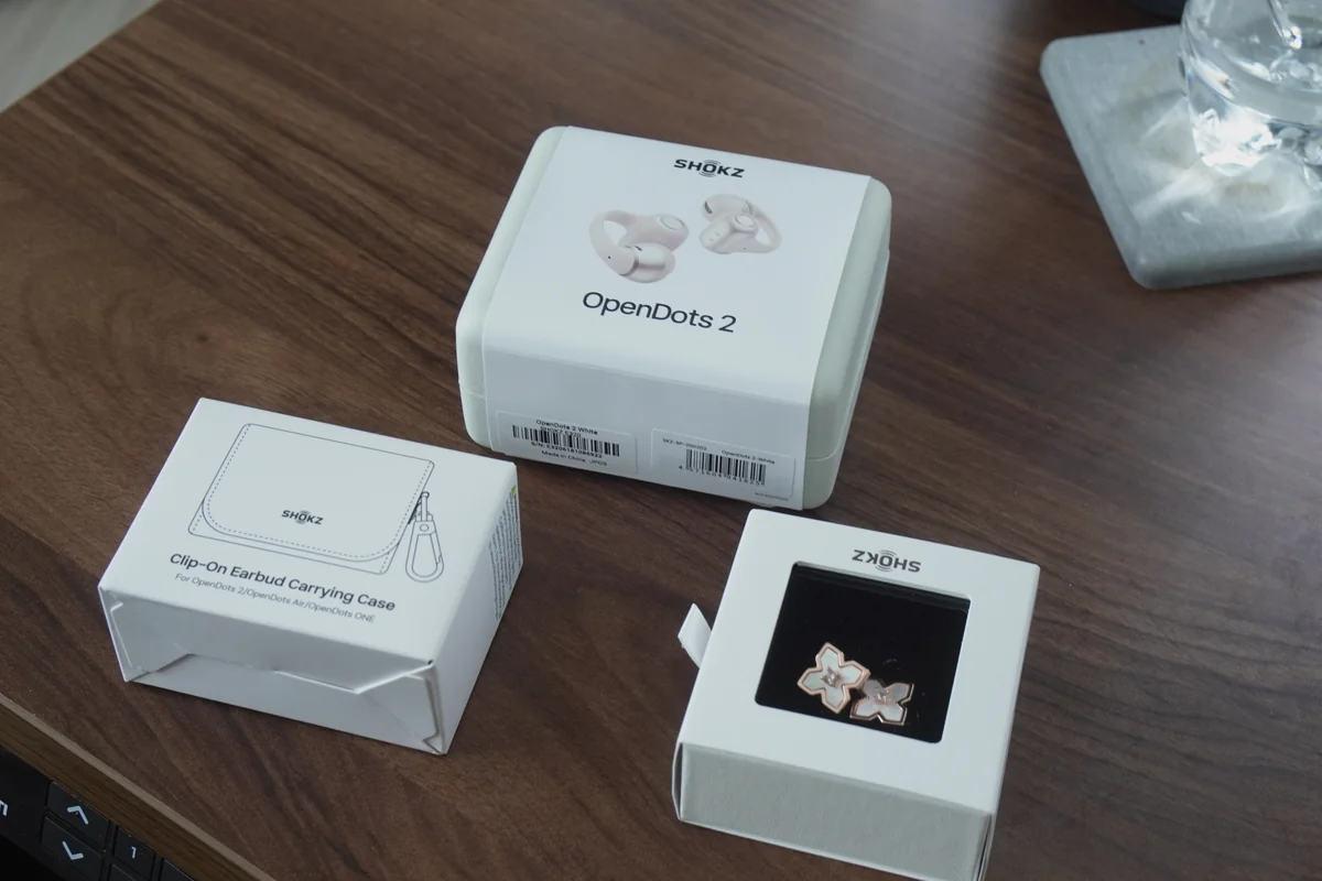 Shokz OpenDots 2本体パッケージとクリップオンケース・チャームアクセサリーを木製デスクに並べた様子