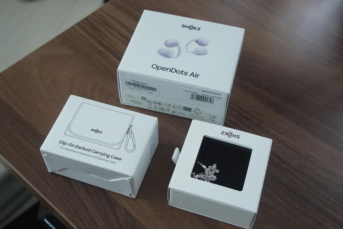 Shokz OpenDots Airの本体パッケージとクリップオンケース、フラワーチャームを木製テーブルに並べた様子