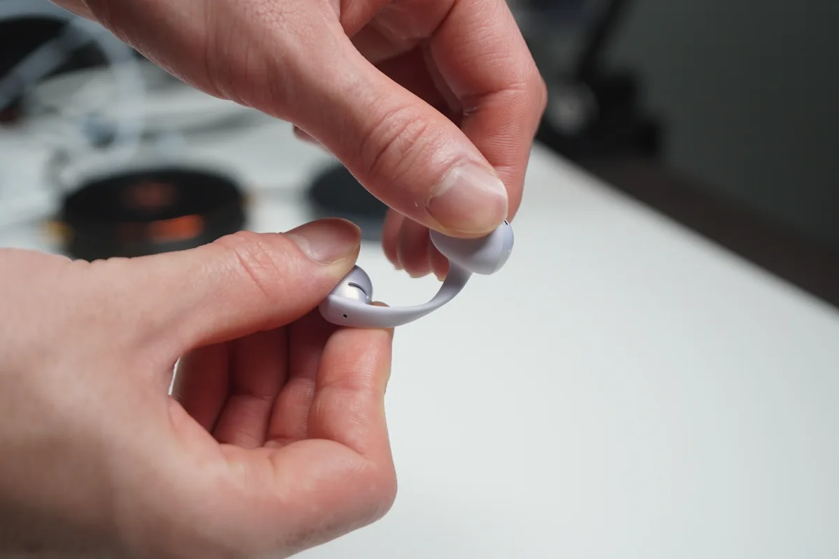 Shokz OpenDots Airのパープル本体イヤホンを指でつまんで形状を見せた様子